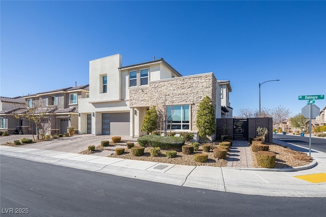 view of front of property featuring driveway, stone siding, a residential view, an attached garage, and stucco siding