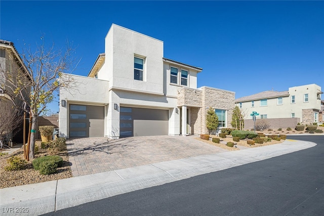 contemporary home with stone siding, decorative driveway, an attached garage, and stucco siding