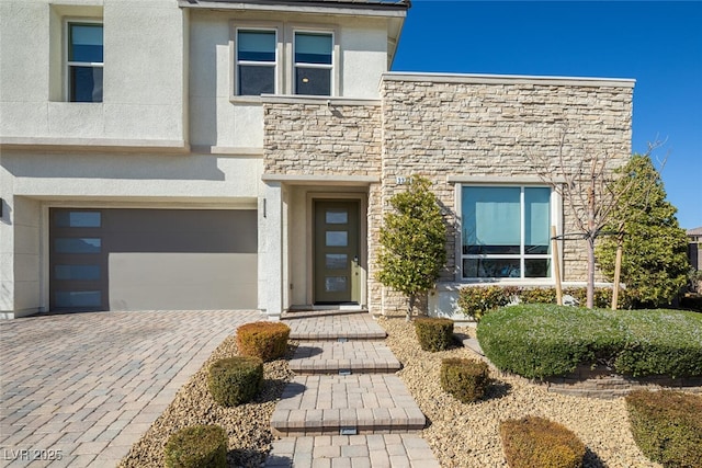 view of front of home featuring a garage, stone siding, decorative driveway, and stucco siding