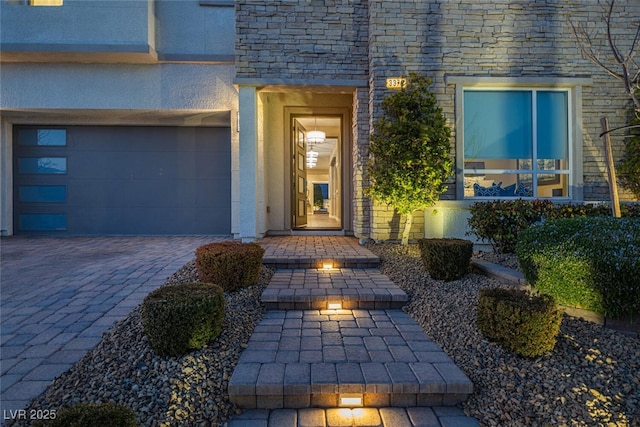 property entrance featuring a garage, decorative driveway, and stucco siding