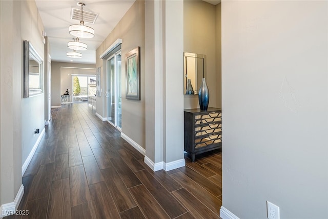 hall featuring dark wood-style flooring, visible vents, and baseboards