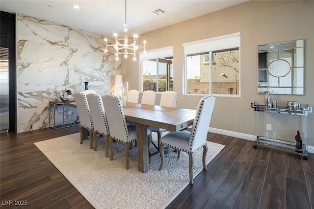 dining area featuring a chandelier, an accent wall, dark wood-style flooring, and visible vents