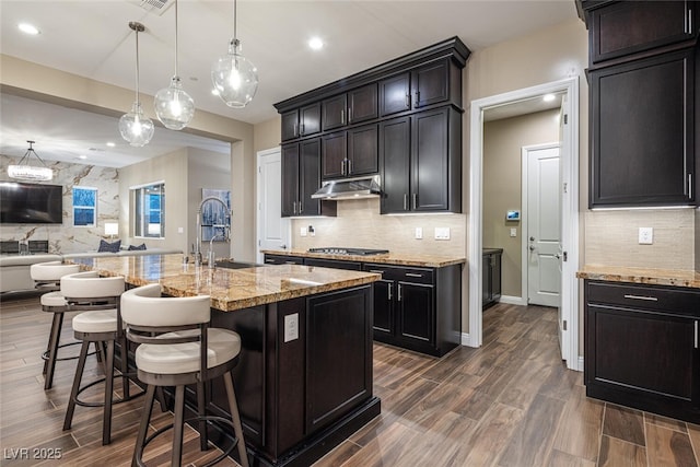 kitchen featuring open floor plan, a kitchen breakfast bar, wood tiled floor, under cabinet range hood, and a sink