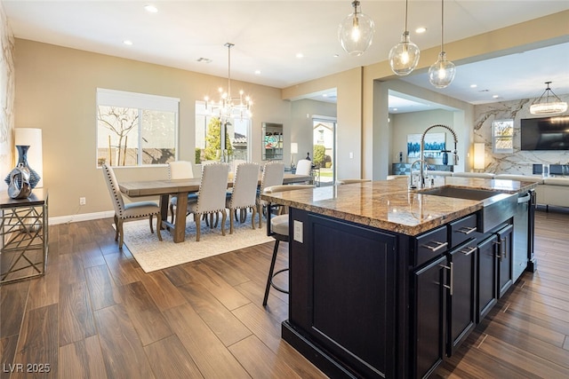 kitchen featuring open floor plan, dark wood-style flooring, dark cabinets, light stone countertops, and a sink