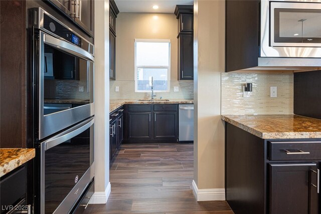 kitchen with a sink, baseboards, appliances with stainless steel finishes, decorative backsplash, and dark wood finished floors