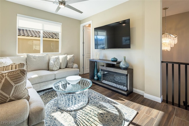 living area with wood tiled floor, baseboards, and ceiling fan with notable chandelier