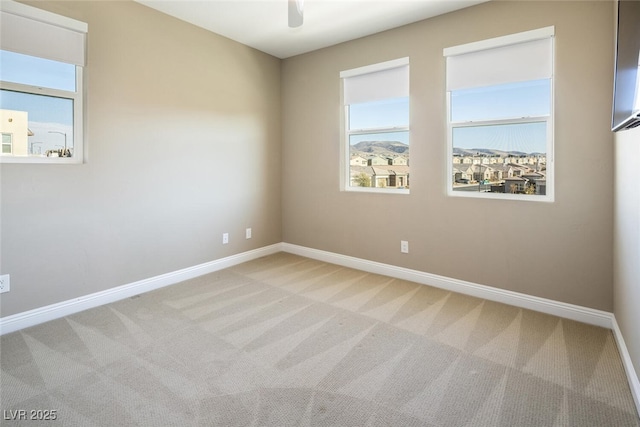 carpeted spare room with a ceiling fan and baseboards