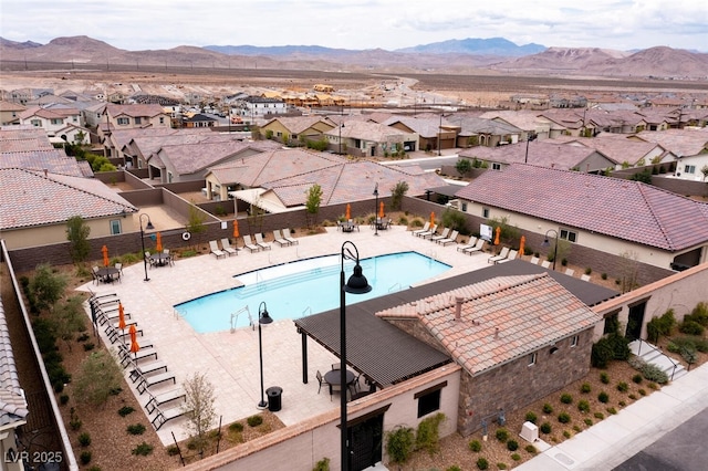 community pool with a residential view, a mountain view, fence, and a patio