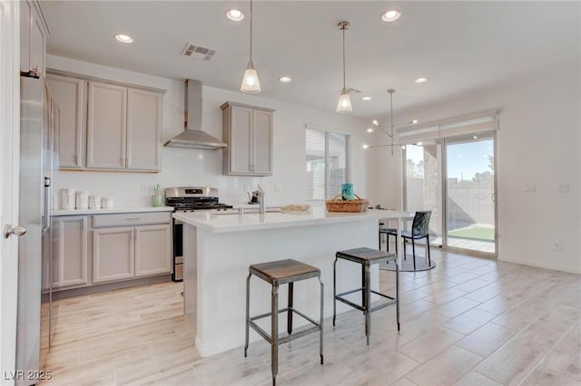 kitchen featuring appliances with stainless steel finishes, hanging light fixtures, a center island with sink, a kitchen bar, and wall chimney exhaust hood