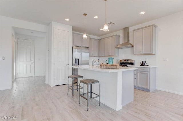 kitchen featuring gray cabinetry, light hardwood / wood-style flooring, appliances with stainless steel finishes, a kitchen island with sink, and wall chimney range hood