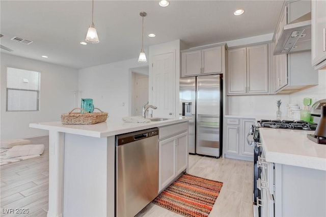 kitchen with hanging light fixtures, appliances with stainless steel finishes, a kitchen island with sink, and light wood-type flooring