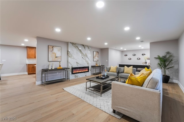 living area featuring baseboards, a premium fireplace, recessed lighting, and light wood-style floors