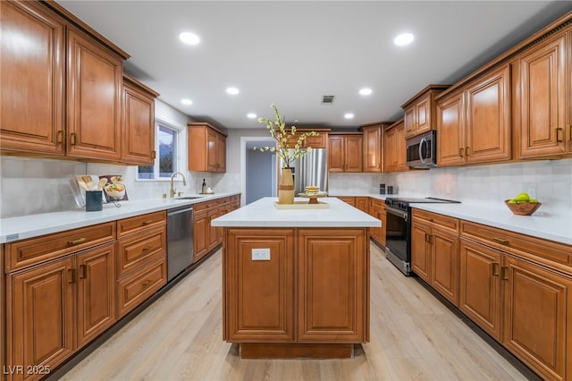 kitchen with a center island, brown cabinets, light countertops, appliances with stainless steel finishes, and a sink