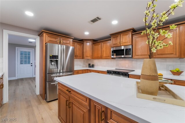 kitchen with recessed lighting, stainless steel appliances, visible vents, backsplash, and brown cabinetry