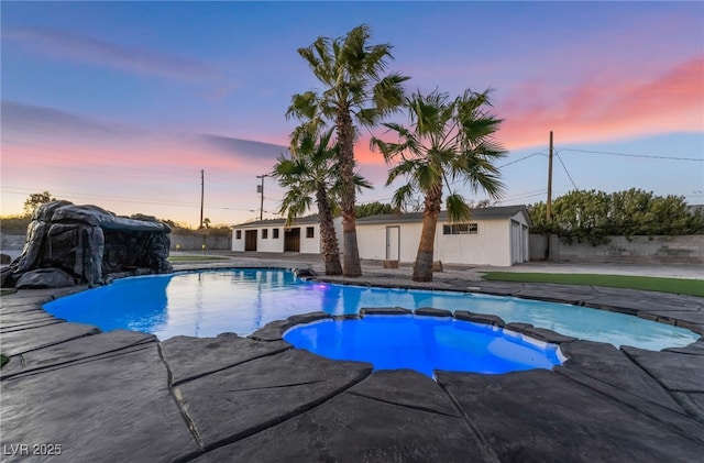 pool at dusk with fence and a pool with connected hot tub