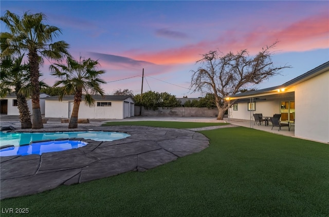 pool at dusk with an outdoor pool, a yard, and a patio