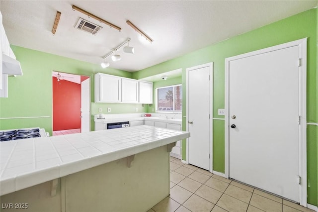 kitchen featuring stainless steel dishwasher, tile counters, white cabinets, and light tile patterned floors