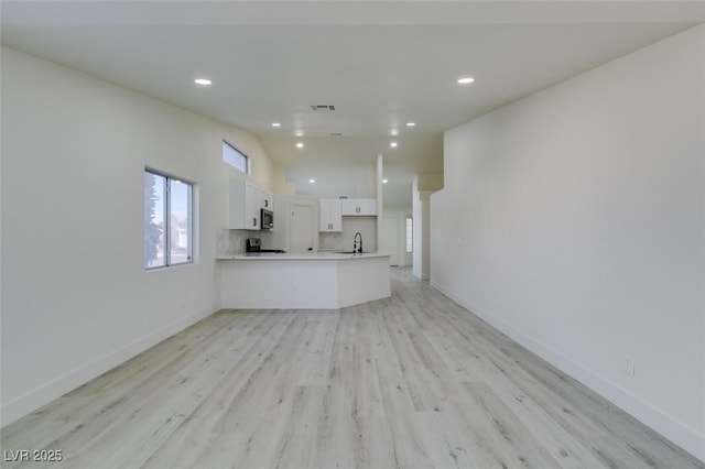 unfurnished living room featuring lofted ceiling, sink, and light hardwood / wood-style flooring