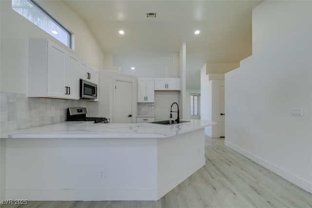 kitchen featuring appliances with stainless steel finishes, white cabinetry, sink, kitchen peninsula, and light stone countertops