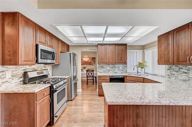 kitchen featuring sink, stainless steel appliances, light stone counters, light hardwood / wood-style floors, and kitchen peninsula