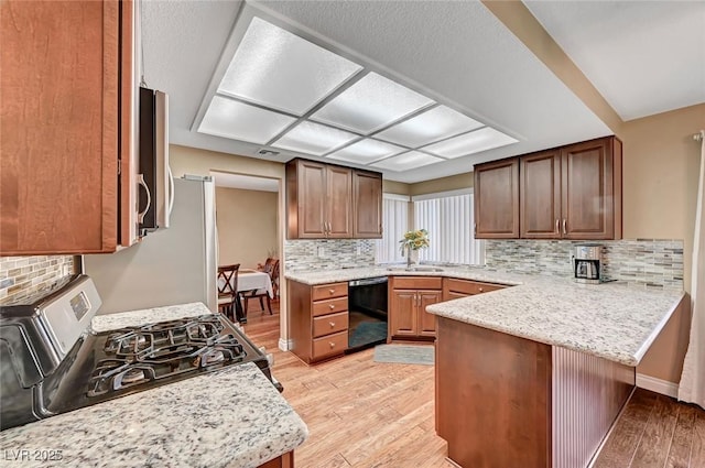 kitchen featuring black dishwasher, stainless steel stove, light hardwood / wood-style floors, and kitchen peninsula