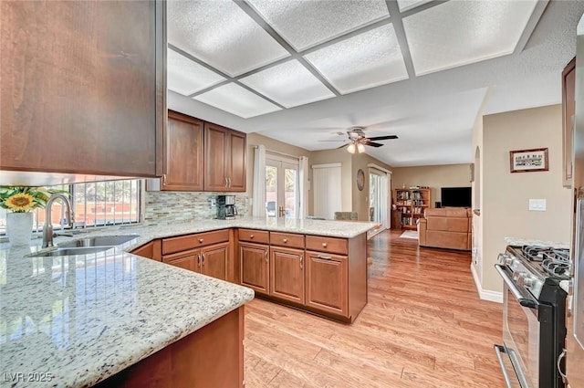 kitchen with sink, light wood-type flooring, stainless steel range with gas cooktop, kitchen peninsula, and light stone countertops