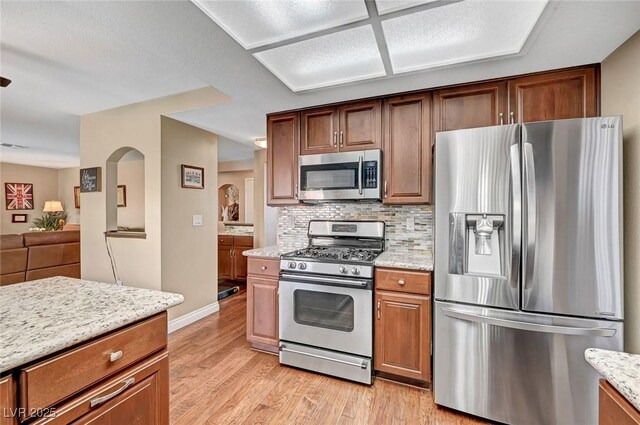 kitchen with light stone counters, decorative backsplash, stainless steel appliances, and light hardwood / wood-style floors