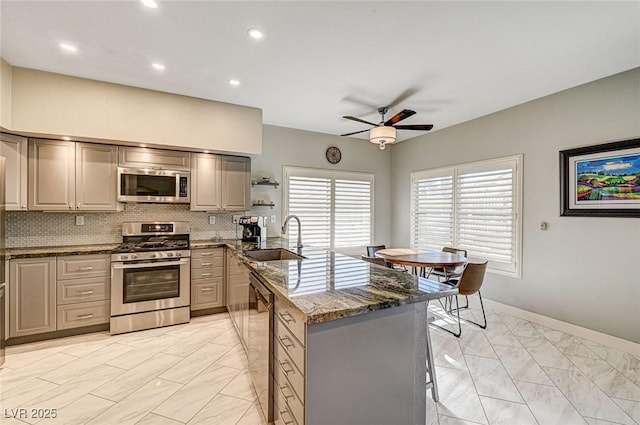 kitchen with sink, ceiling fan, stainless steel appliances, decorative backsplash, and dark stone counters