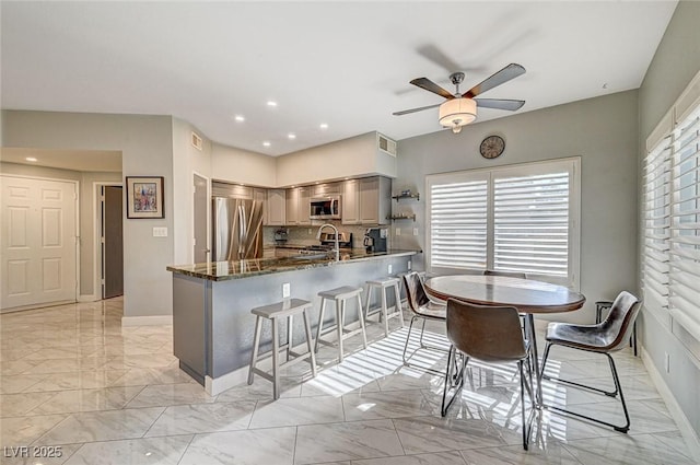 kitchen with sink, a breakfast bar area, appliances with stainless steel finishes, dark stone countertops, and kitchen peninsula