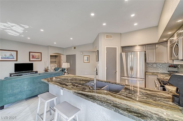 kitchen with sink, a breakfast bar area, appliances with stainless steel finishes, stone counters, and backsplash