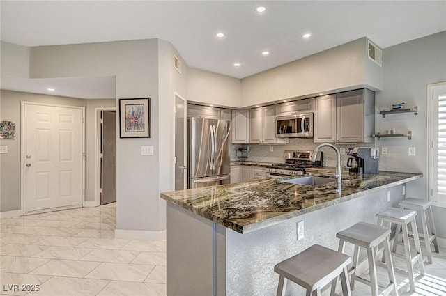 kitchen featuring gray cabinetry, stainless steel appliances, kitchen peninsula, and dark stone counters