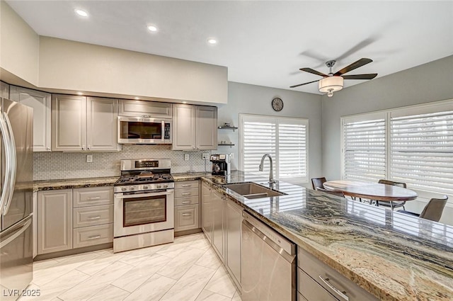 kitchen with appliances with stainless steel finishes, sink, dark stone countertops, decorative backsplash, and ceiling fan