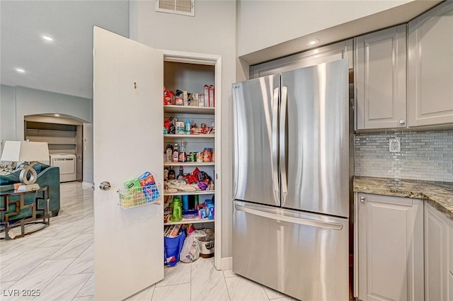 kitchen with tasteful backsplash, light stone countertops, stainless steel refrigerator, and washer / clothes dryer