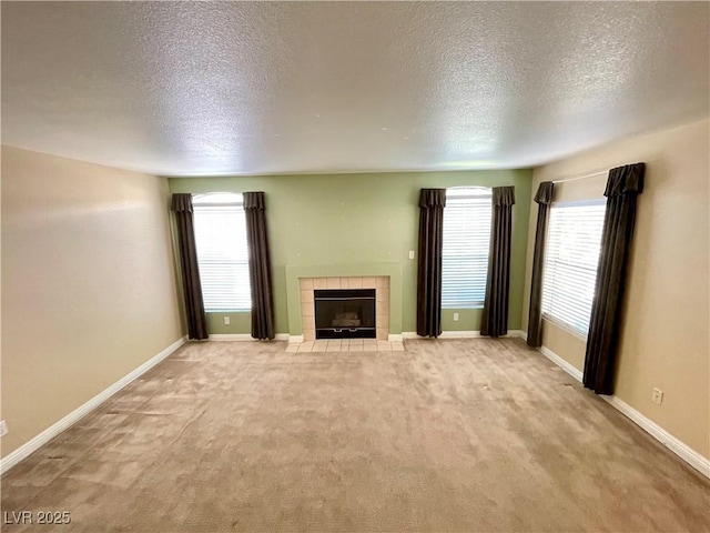 unfurnished living room with light colored carpet, a healthy amount of sunlight, a tiled fireplace, and a textured ceiling