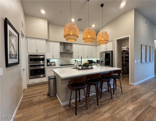 kitchen featuring stainless steel appliances, white cabinetry, pendant lighting, and wall chimney exhaust hood