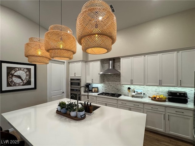 kitchen with sink, tasteful backsplash, a center island with sink, appliances with stainless steel finishes, and wall chimney range hood