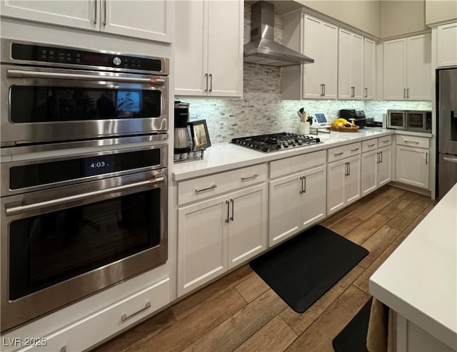 kitchen with stainless steel appliances, tasteful backsplash, wall chimney range hood, and white cabinets