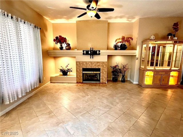 unfurnished living room featuring ceiling fan and a tiled fireplace