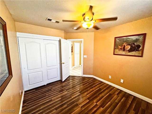 unfurnished bedroom featuring dark wood-type flooring, ceiling fan, a closet, and a textured ceiling