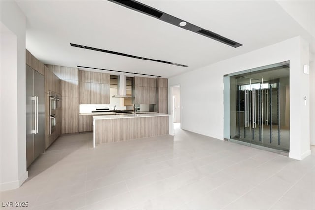 kitchen with stainless steel appliances, an island with sink, and wall chimney exhaust hood