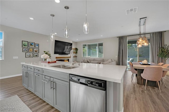 kitchen with gray cabinets, pendant lighting, dishwasher, an island with sink, and sink