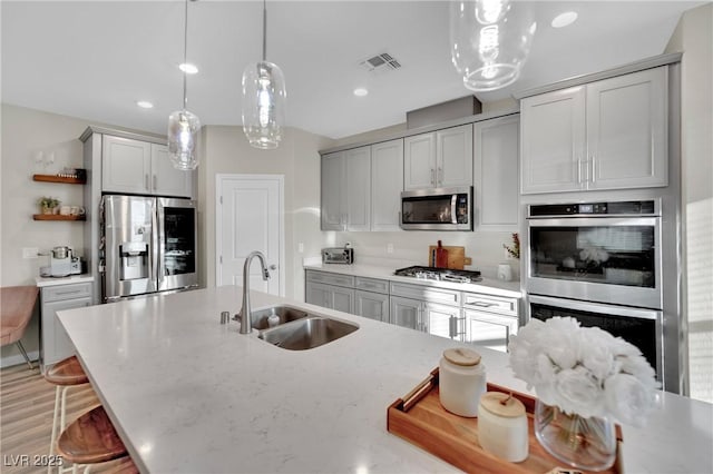 kitchen with a kitchen bar, sink, decorative light fixtures, gray cabinets, and stainless steel appliances