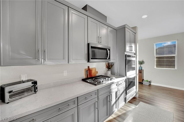 kitchen with stainless steel appliances, light stone countertops, gray cabinets, and dark wood-type flooring