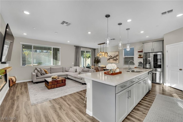 kitchen featuring an island with sink, sink, gray cabinetry, hanging light fixtures, and stainless steel appliances