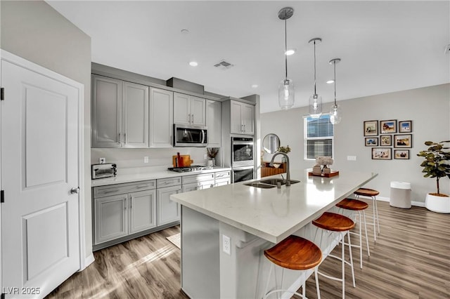 kitchen featuring stainless steel appliances, sink, gray cabinetry, and a kitchen island with sink