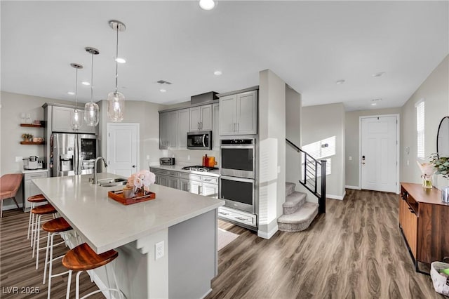 kitchen featuring gray cabinetry, hanging light fixtures, a kitchen breakfast bar, stainless steel appliances, and a kitchen island with sink