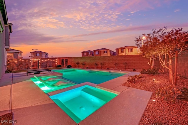 pool at dusk featuring an in ground hot tub and a patio area