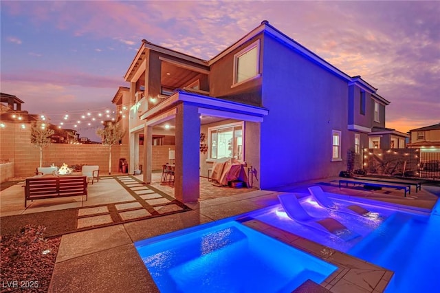 pool at dusk with an outdoor living space, a patio area, and an in ground hot tub