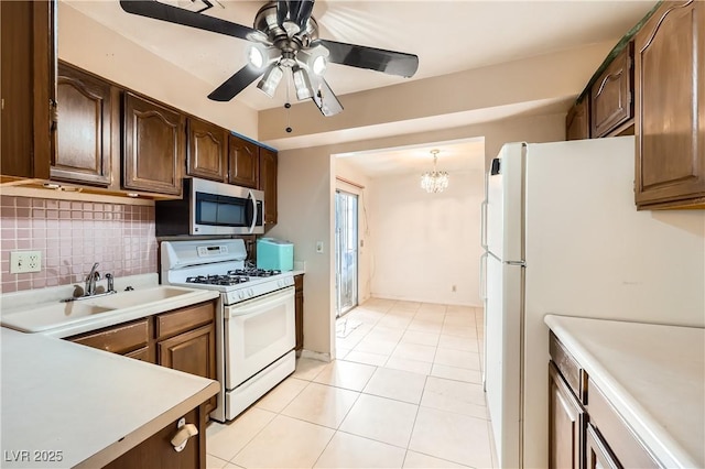 kitchen featuring hanging light fixtures, light tile patterned floors, white appliances, ceiling fan with notable chandelier, and backsplash