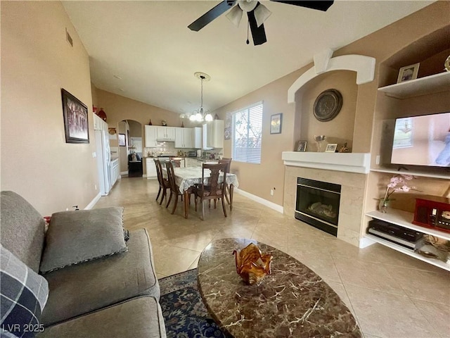 tiled living room featuring lofted ceiling, a tiled fireplace, and ceiling fan with notable chandelier